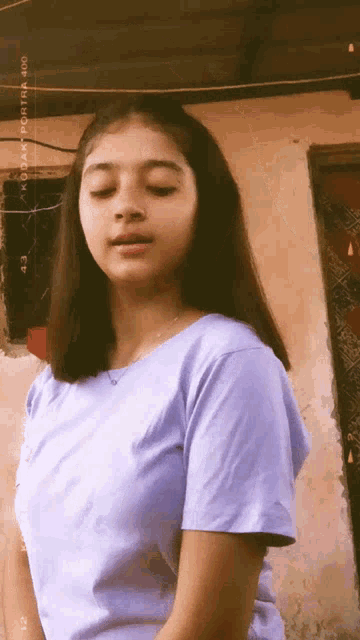 a girl in a purple shirt is standing in front of a wall with kodak written on it