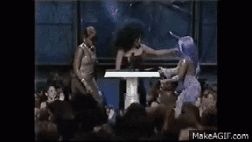 a group of women are standing around a table in front of a crowd of people .