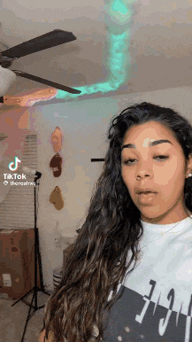 a woman with long hair is standing in a room with a ceiling fan in the background .