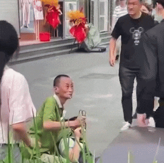 a man in a green shirt is sitting on the sidewalk next to a woman in a black shirt .