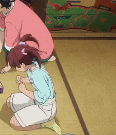 a girl is kneeling down on the floor while a man sits behind her