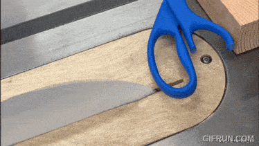 a pair of scissors cutting a piece of wood on a table saw