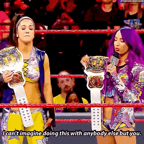 two women are standing in a wrestling ring holding their championship belts .