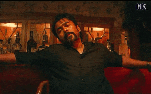 a man is sitting at a bar with his arms outstretched in front of a bar full of bottles of alcohol .