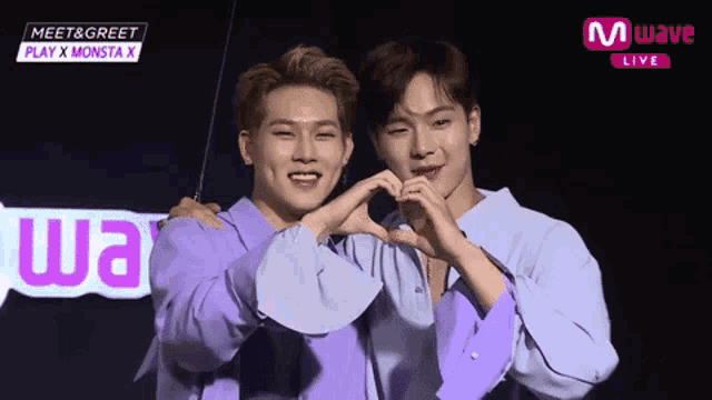 two young men in purple shirts are making a heart shape with their hands