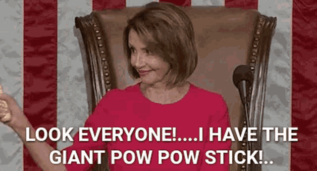 a woman in a red dress is sitting in a chair in front of a microphone and holding a giant pow pow stick .
