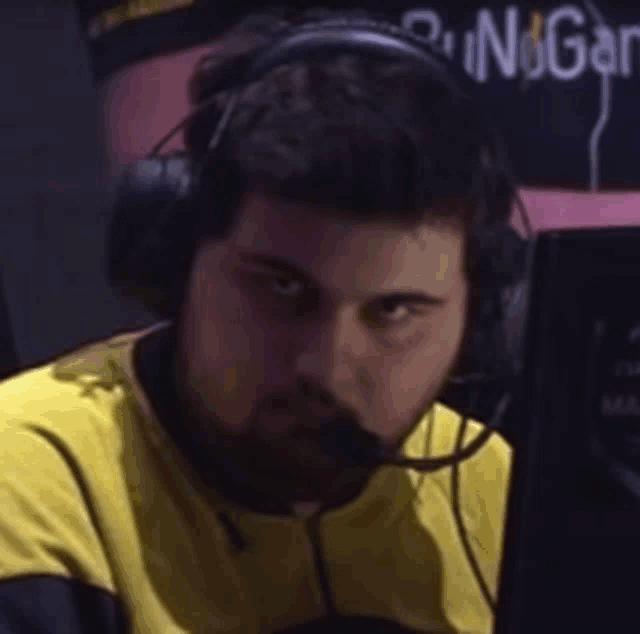 a man wearing headphones and a yellow shirt is looking at a computer monitor