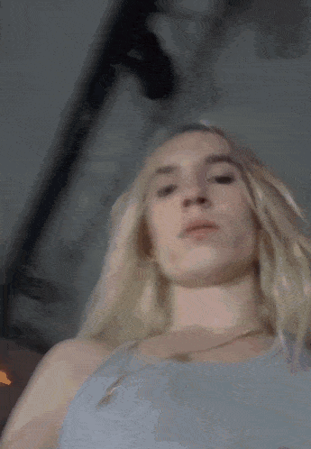 a woman with blonde hair is wearing a blue tank top and a gold necklace .