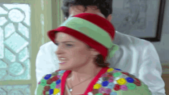 a woman wearing a red hat and a green scarf stands next to a man