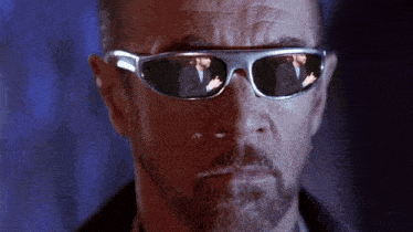 a man wearing sunglasses has a reflection of another man in the glasses