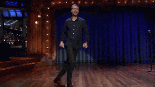 a man in a suit is dancing on a stage with a blue curtain behind him
