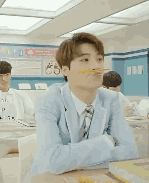 a boy in a suit has a pencil in his mouth while sitting at a desk