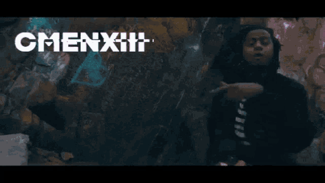 a man in a black hoodie is standing in front of a wall with the word omenxiii on it