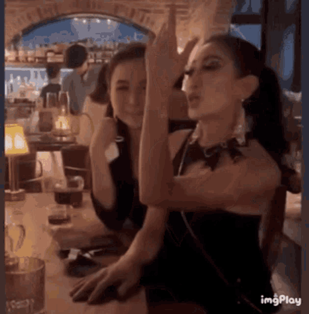 two women are sitting at a table in a bar and one of them is pointing