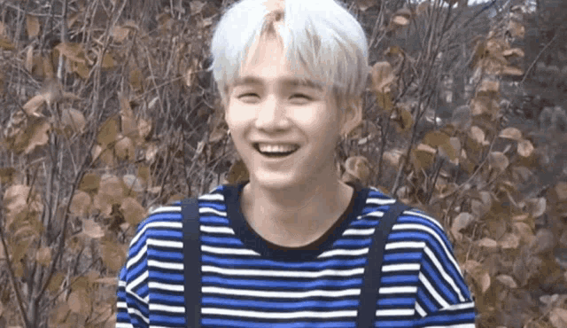 a young man with white hair wearing a blue and white striped shirt and suspenders is smiling .