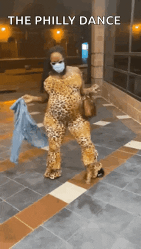 a woman wearing a face mask and a leopard print jumpsuit is dancing on a tiled floor .