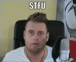 a man in a white shirt is sitting in front of a microphone with the word stfu written on his face .