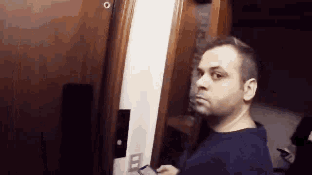 a man in a blue shirt is standing in front of a door holding a cell phone
