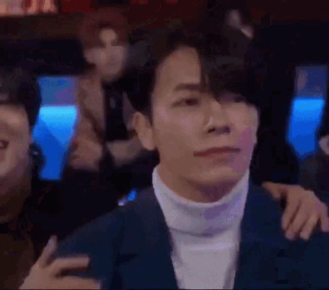 a man in a blue suit and white turtleneck is sitting in a crowd of people .