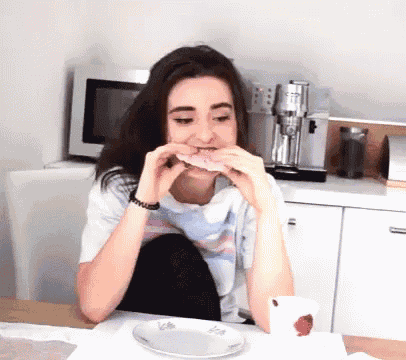 a woman is sitting at a table eating a sandwich with a cup of tea in front of her
