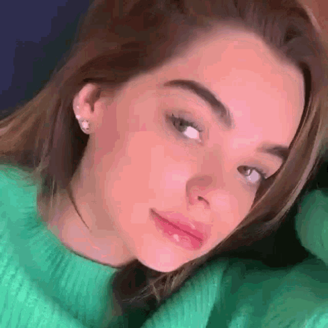 a woman in a green sweater is looking at the camera .