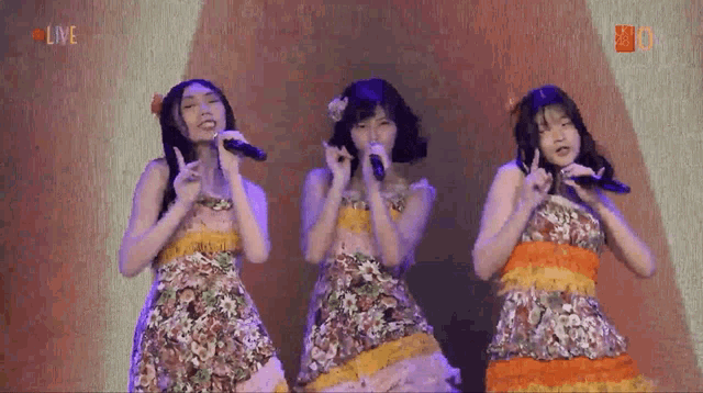 three girls singing into microphones with the word live in the upper right corner