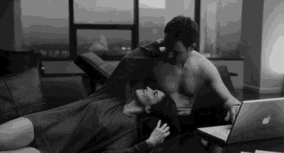 a man and a woman are kissing while laying on a couch next to a laptop .