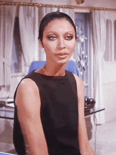 a woman in a black dress is sitting in a room looking at the camera