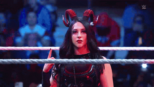 a woman with horns is standing in a wrestling ring and giving a middle finger .