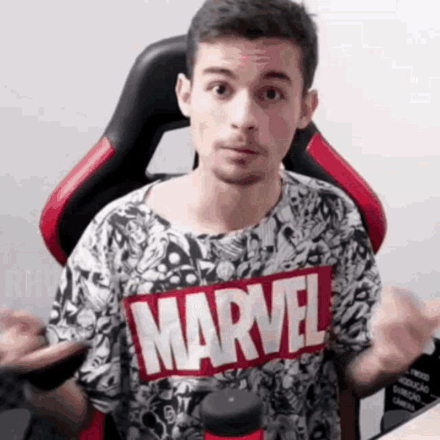 a man wearing a marvel t-shirt is sitting in a red and black chair .