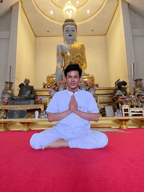 a man sits in front of a buddha statue with his hands folded in front of him