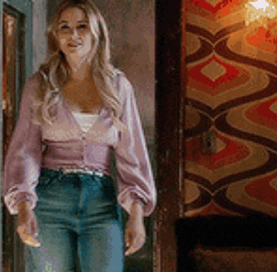 a woman is standing in a hallway wearing a purple sweater and jeans .