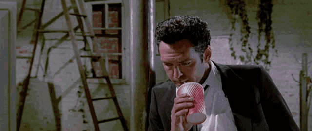 a man in a suit is drinking from a red and white cup