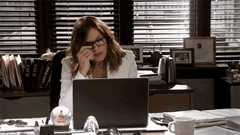 a woman wearing glasses is sitting at a desk with a laptop and talking on her phone