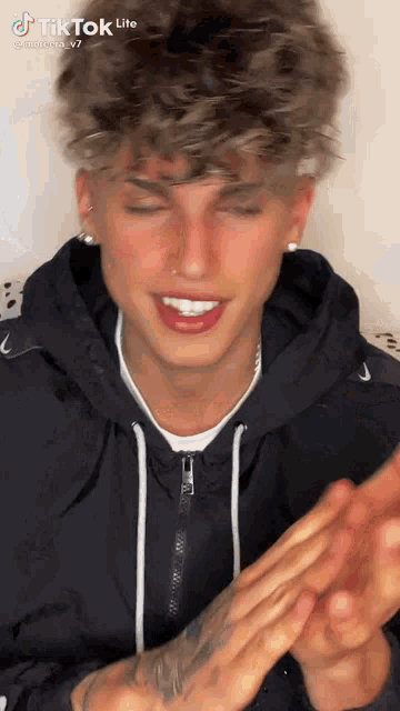 a young man wearing a black hoodie is clapping his hands and smiling .