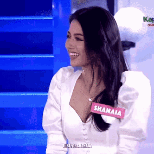a woman wearing a white shirt with a name tag that says shanaia is smiling .