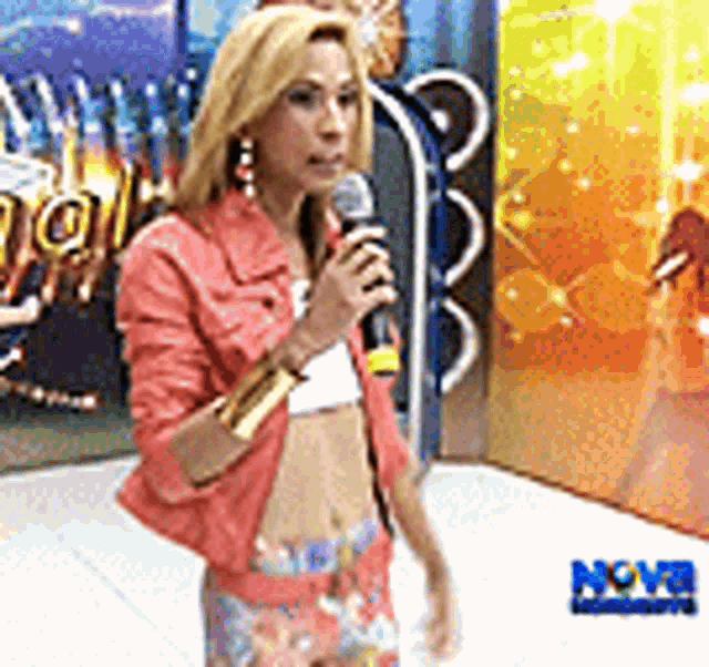 a woman in a pink jacket is holding a microphone in front of a nova advertisement .