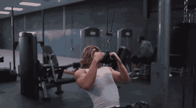 a man in a white tank top is using a machine in the gym