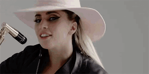 lady gaga is wearing a pink hat and a leather jacket while singing into a microphone .