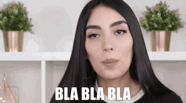 a woman with long black hair says bla bla bla in front of some potted plants