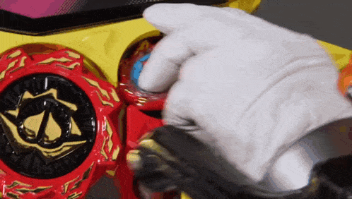 a person wearing a white glove is holding a red and gold toy .