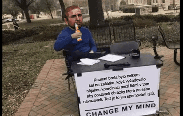 a man sitting at a table with a sign that says change my mind .