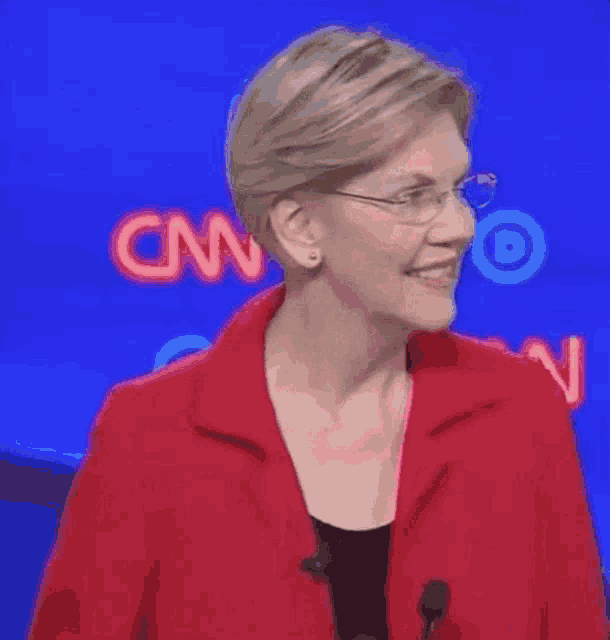 a woman wearing glasses and a red jacket is standing in front of a cnn sign