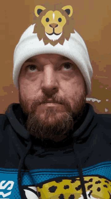 a man with a beard wearing a white beanie with a lion on it