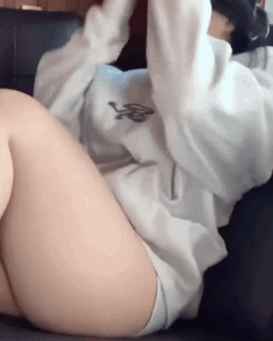a woman is laying on a couch with her legs crossed and a hoodie on .