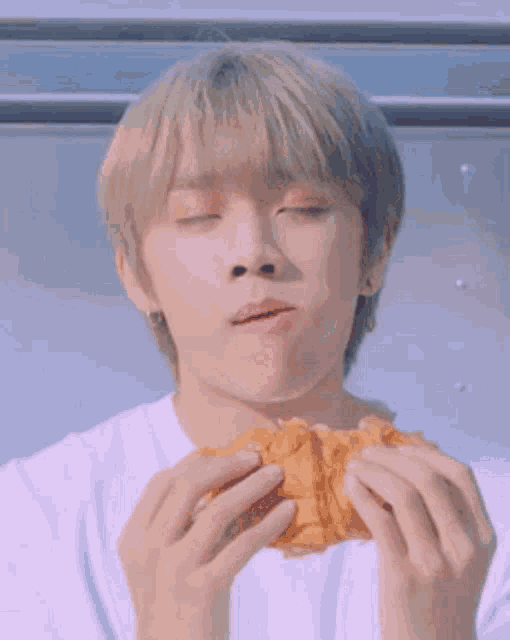 a young man is eating a croissant with his eyes closed and his mouth open .