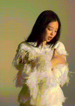 a woman in a white dress with feathers on the sleeves is standing in front of a white background .