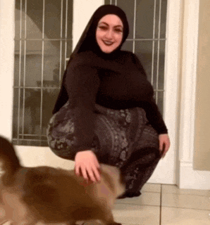 a woman wearing a hijab is kneeling down next to a cat .