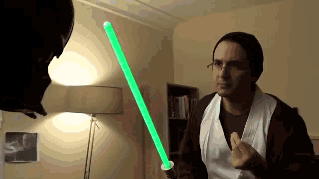 a man is holding a green light saber in front of a darth vader helmet