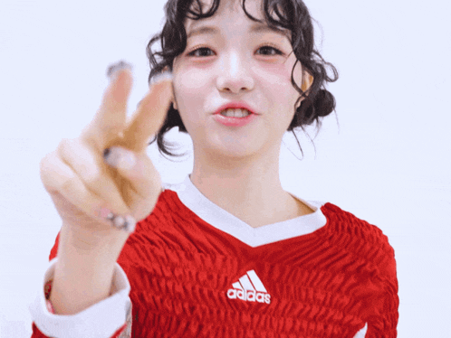 a woman wearing a red adidas shirt is giving the peace sign